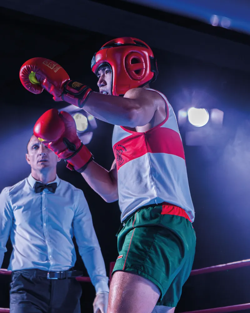 Boxeur au casque rouge en garde haute, l’arbitre en arrière-plan